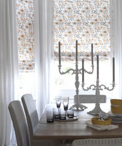 A small touch of pattern on the windows can brighten up a space. Roman shades in a modern floral fabric keep a wood table and wicker chairs from feeling too outdated. Oversized candelabras become a simple, sculptural centerpiece.